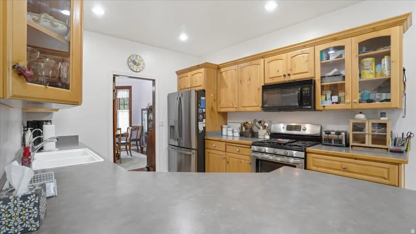 Kitchen featuring glass insert cabinets, stainless steel appliances, light wood finish cabinets, light countertops, and recessed lighting