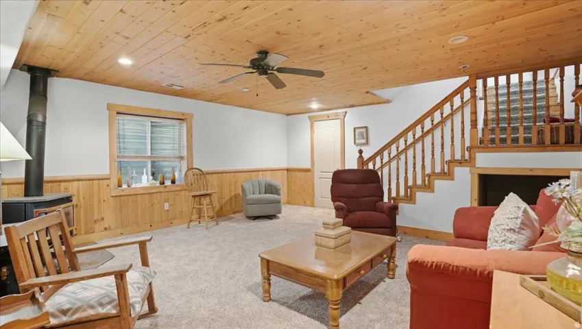 Living area with a wood stove, wooden walls, wood ceiling, a wainscoted wall, and a ceiling fan