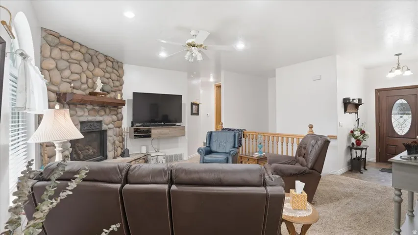 Living room featuring a ceiling fan, a fireplace, carpet, and hanging lights
