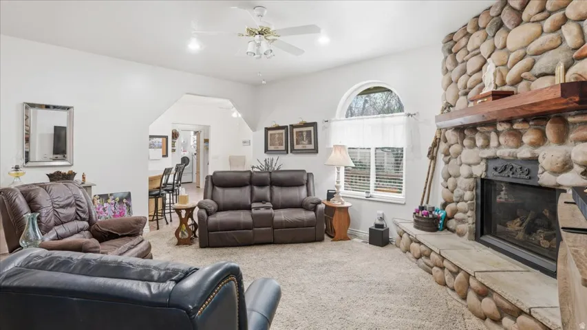 Living room featuring carpet, a fireplace, and a ceiling fan