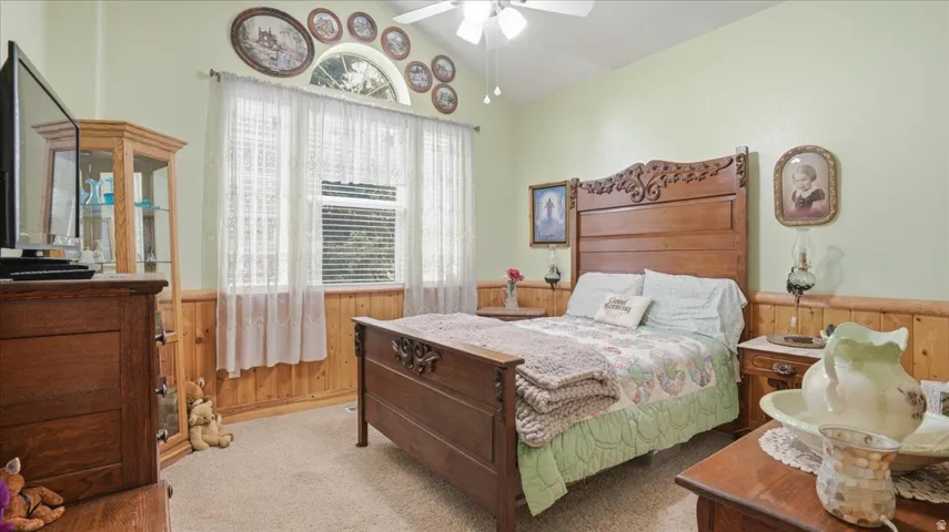 Carpeted bedroom featuring wood walls, wainscoting, vaulted ceiling, and a ceiling fan