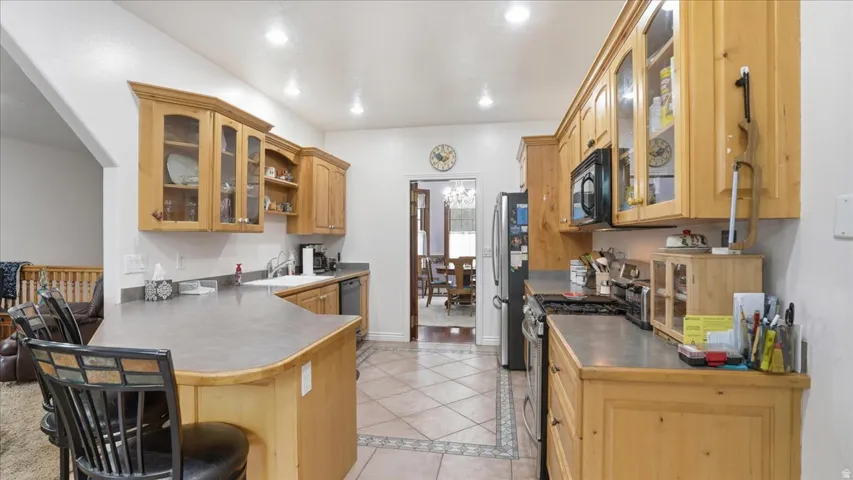 Kitchen featuring glass fronted cabinets, stainless steel appliances, a breakfast bar area, light tile patterned floors, and inlaid floor details