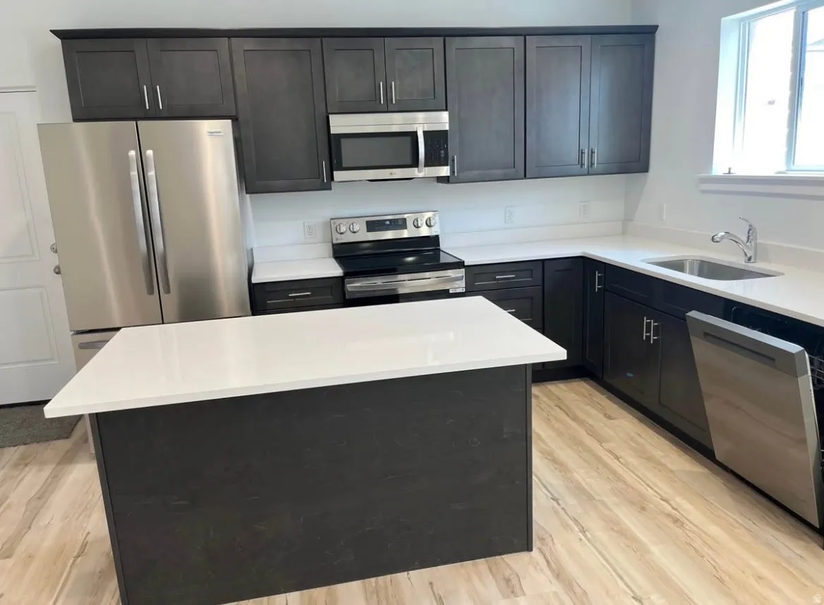 Kitchen featuring stainless steel appliances, dark cabinets, a kitchen island, and light stone counters