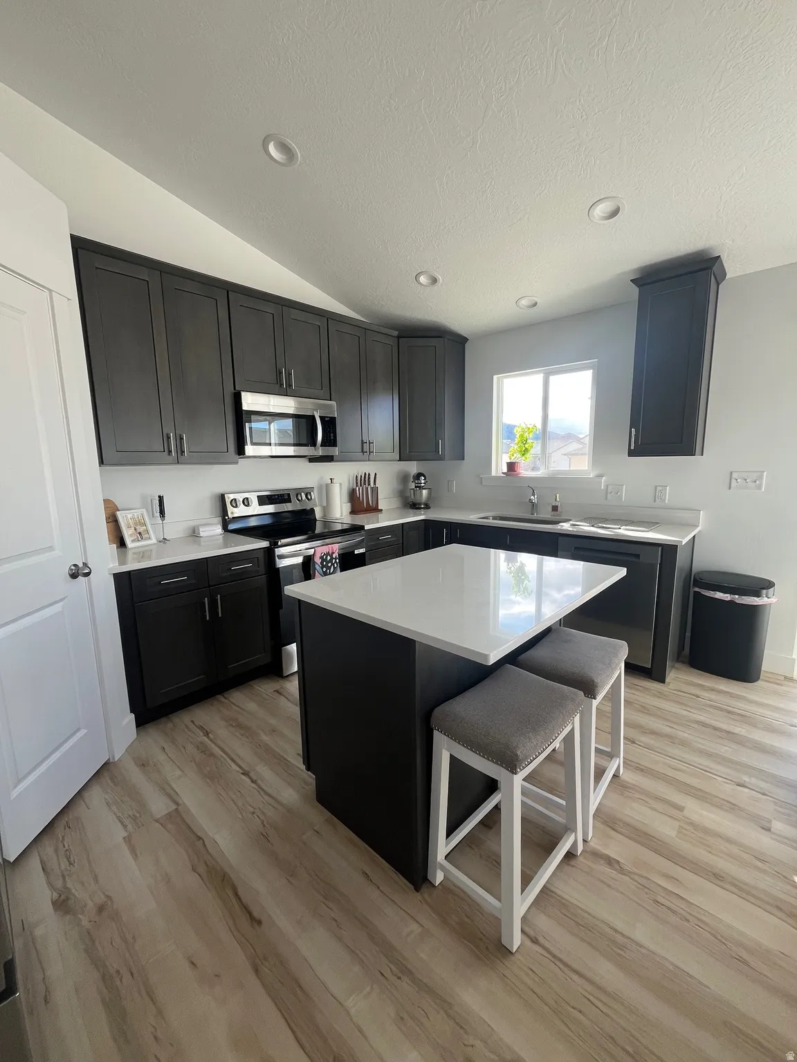 Kitchen with stainless steel appliances, a kitchen island, dark cabinetry, a breakfast bar area, and recessed lighting