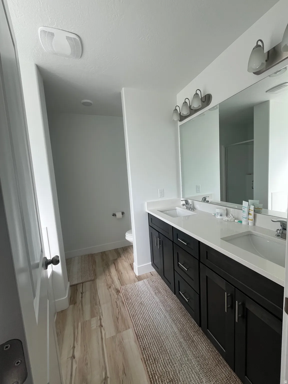 Full bathroom with double vanity, a shower stall, light wood-style flooring, and a textured ceiling