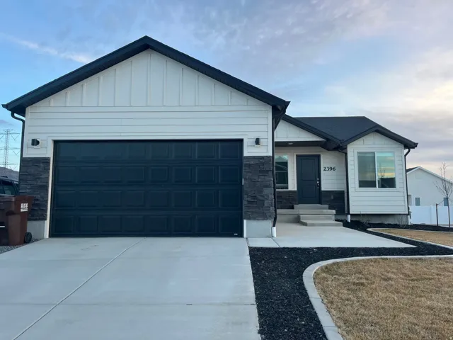 View of front of home with an attached garage, stone siding, board and batten siding, and concrete driveway