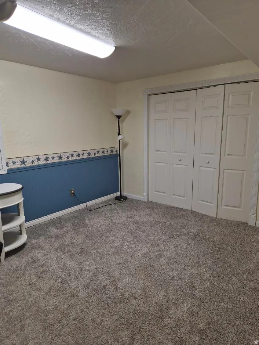 Unfurnished bedroom featuring a wainscoted wall, carpet, a textured ceiling, and a closet