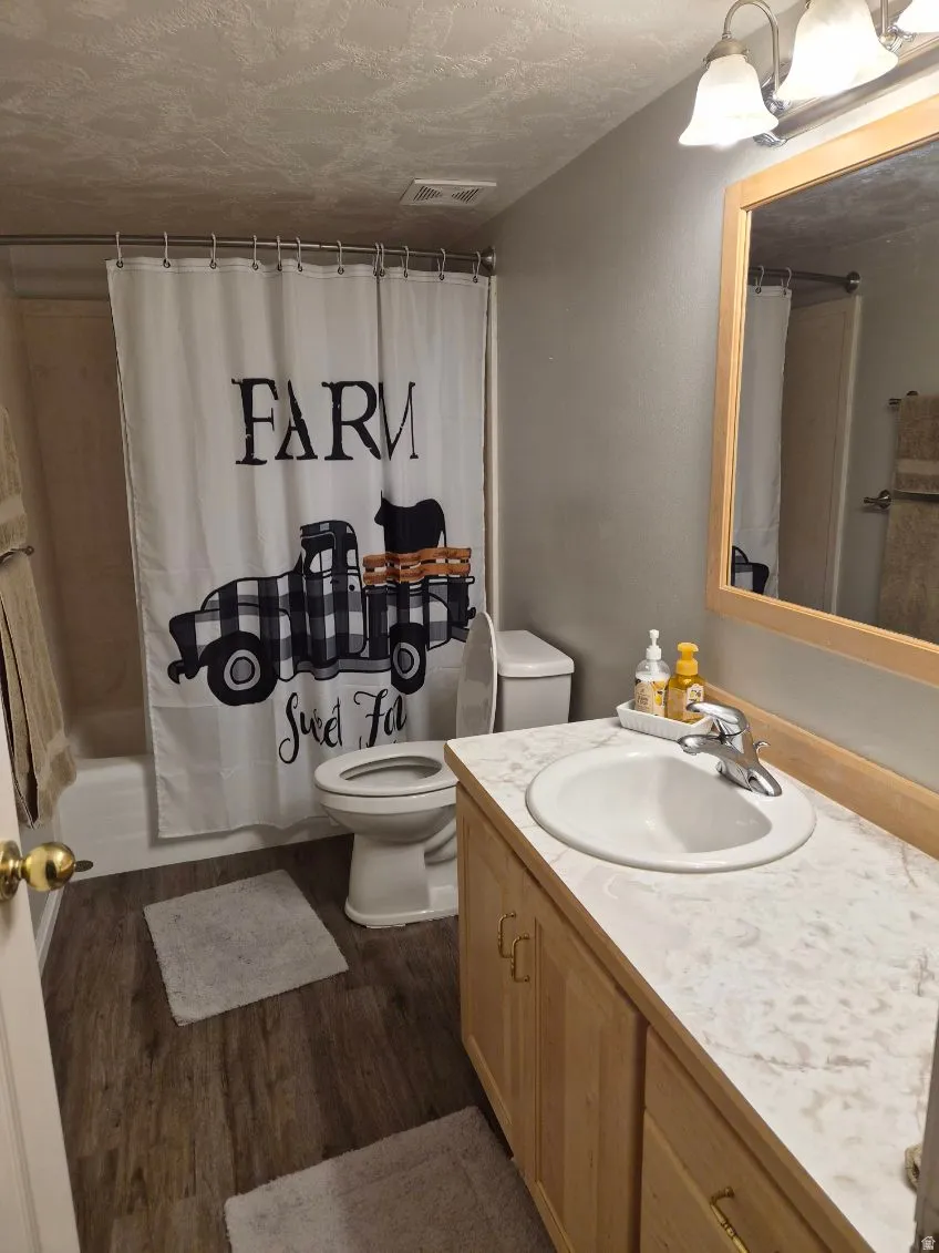 Full bathroom featuring vanity, shower / tub combo with curtain, dark wood-style floors, and a textured ceiling