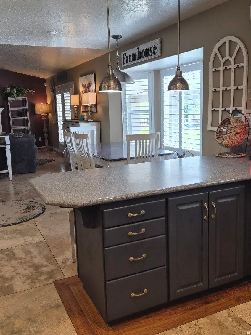 Kitchen featuring dark cabinets, a textured ceiling, open floor plan, hanging light fixtures, and a breakfast bar area
