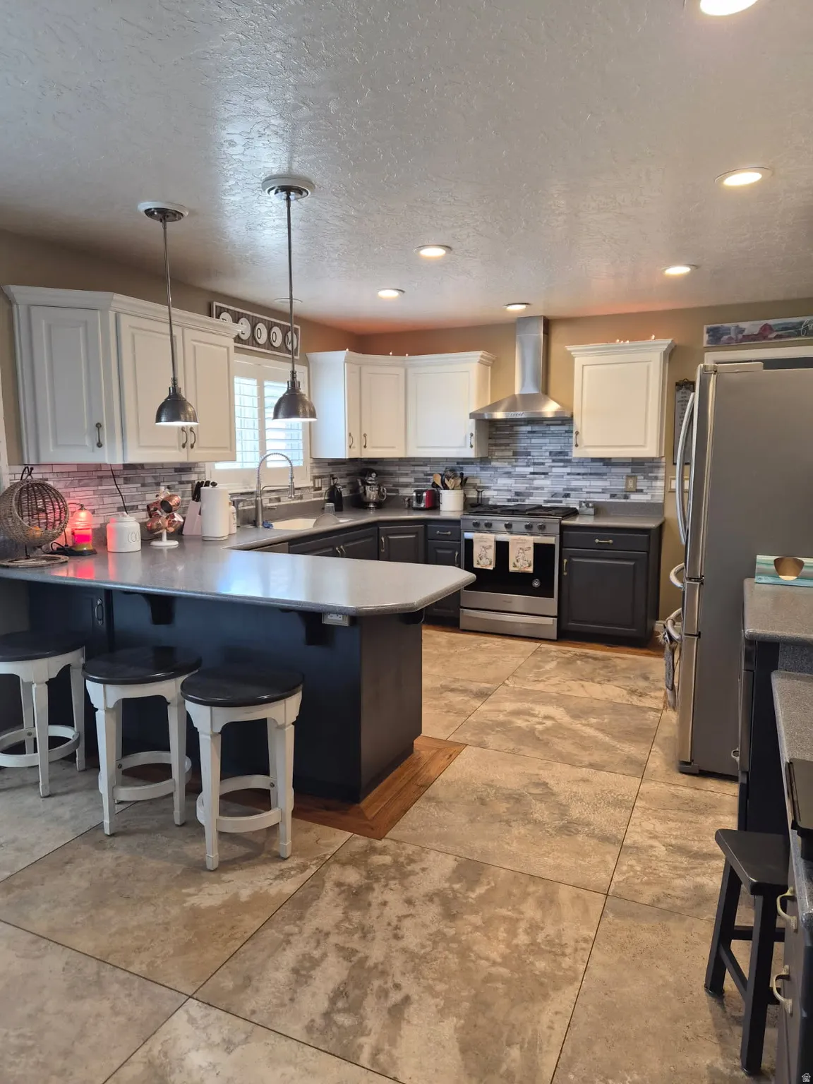 Kitchen featuring a kitchen bar, a peninsula, stainless steel appliances, backsplash, and a textured ceiling