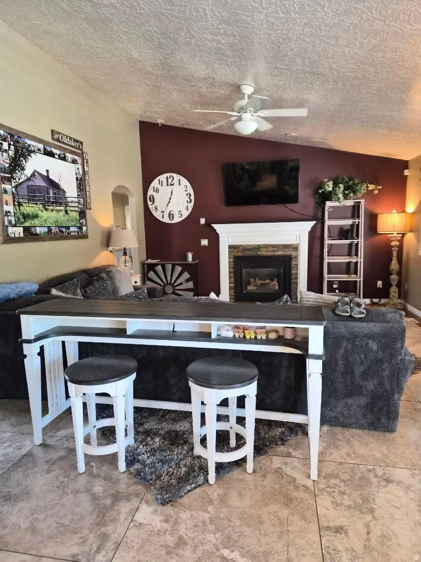 Living room featuring ceiling fan, a fireplace, a textured ceiling, and arched walkways