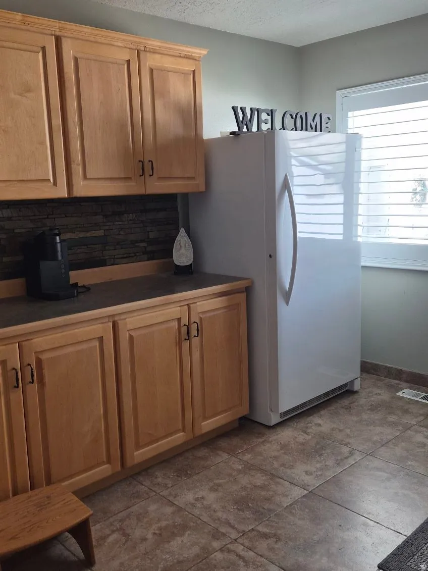 Kitchen featuring dark countertops, freestanding refrigerator, and light wood finish cabinetry
