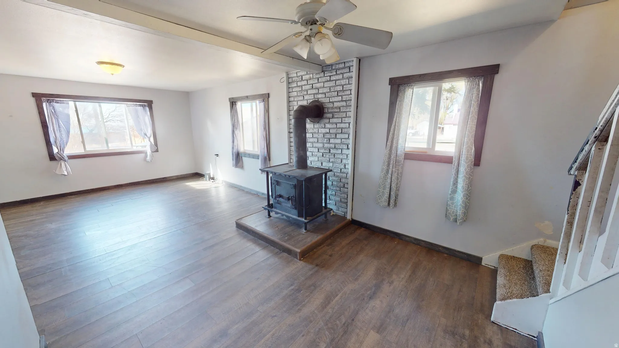 Unfurnished living room with dark wood-style flooring, a wood stove, and a ceiling fan