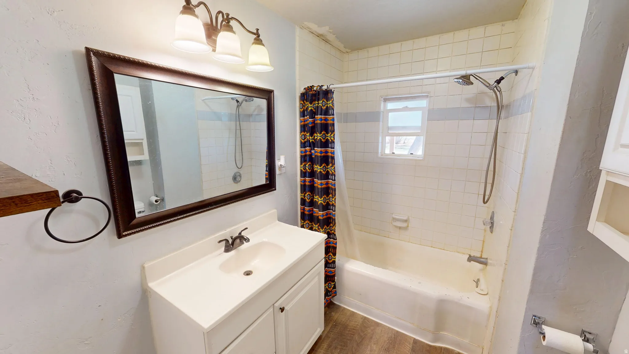 Bathroom featuring vanity, shower / bath combination with curtain, a textured wall, and dark wood-style floors