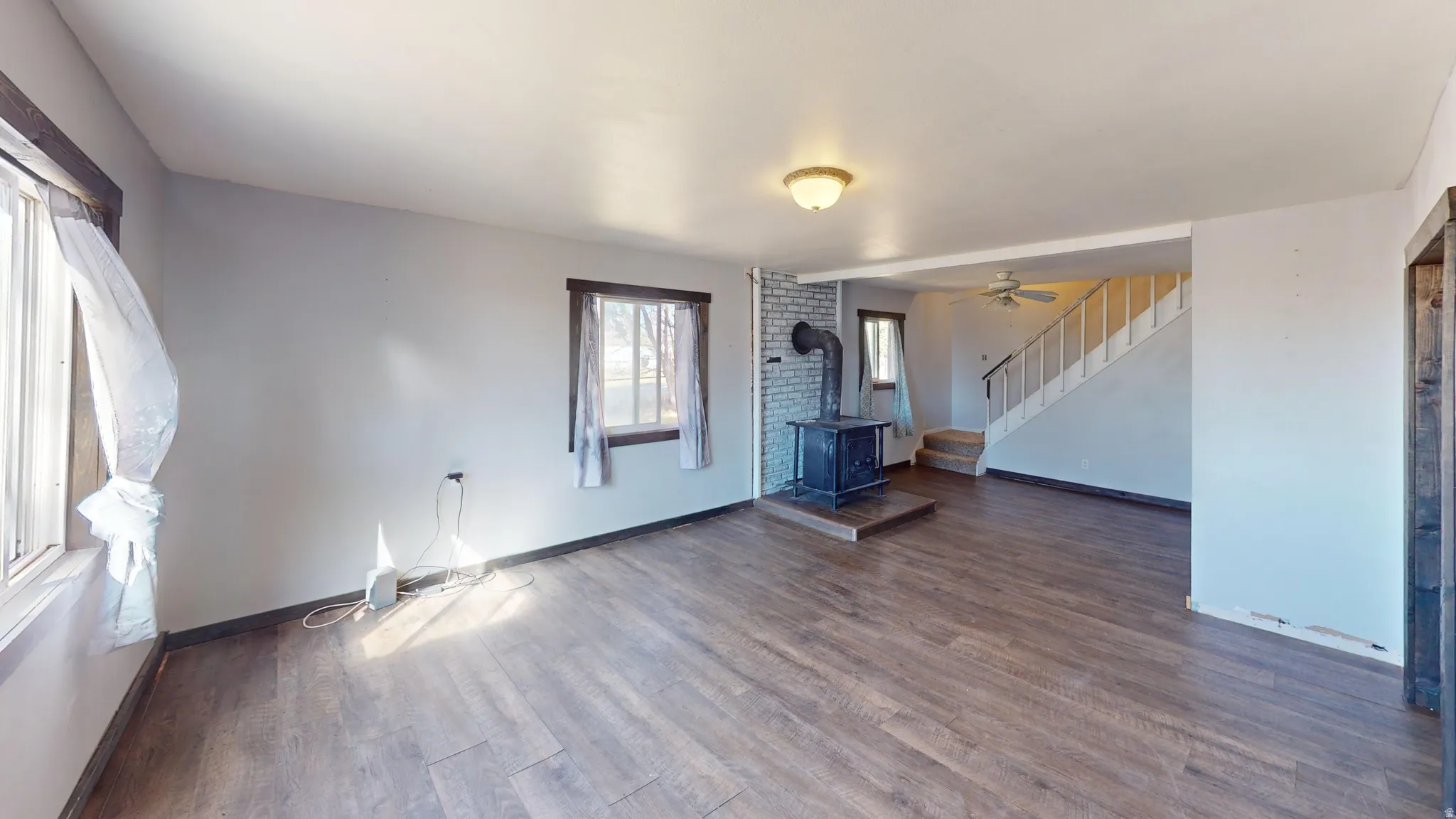 Unfurnished living room featuring a wood stove, dark wood-type flooring, and a ceiling fan