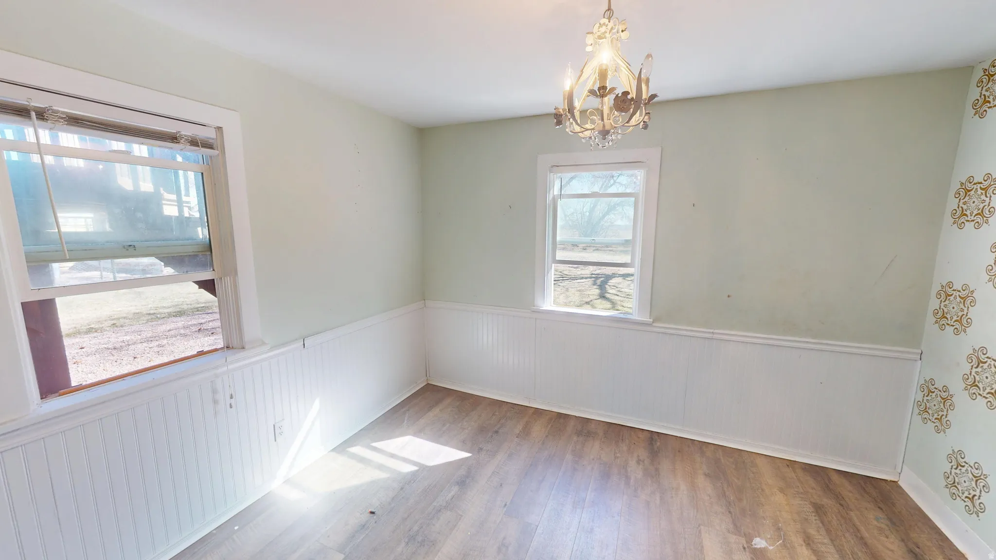 Unfurnished dining area featuring a wainscoted wall, wood finished floors, and suspended lighting