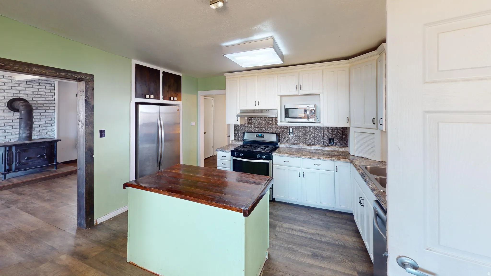 Kitchen with butcher block counters, stainless steel appliances, a kitchen island, tasteful backsplash, and a wood stove