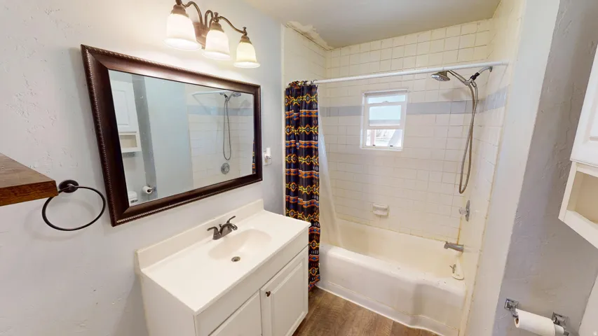 Bathroom featuring vanity, shower / bath combination with curtain, a textured wall, and dark wood-style floors