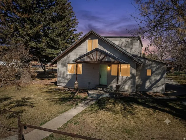 Gray siding exterior featuring a decorative front porch awning with exposed wood beams and stone column accents, a light-colored front door, and a concrete walkway