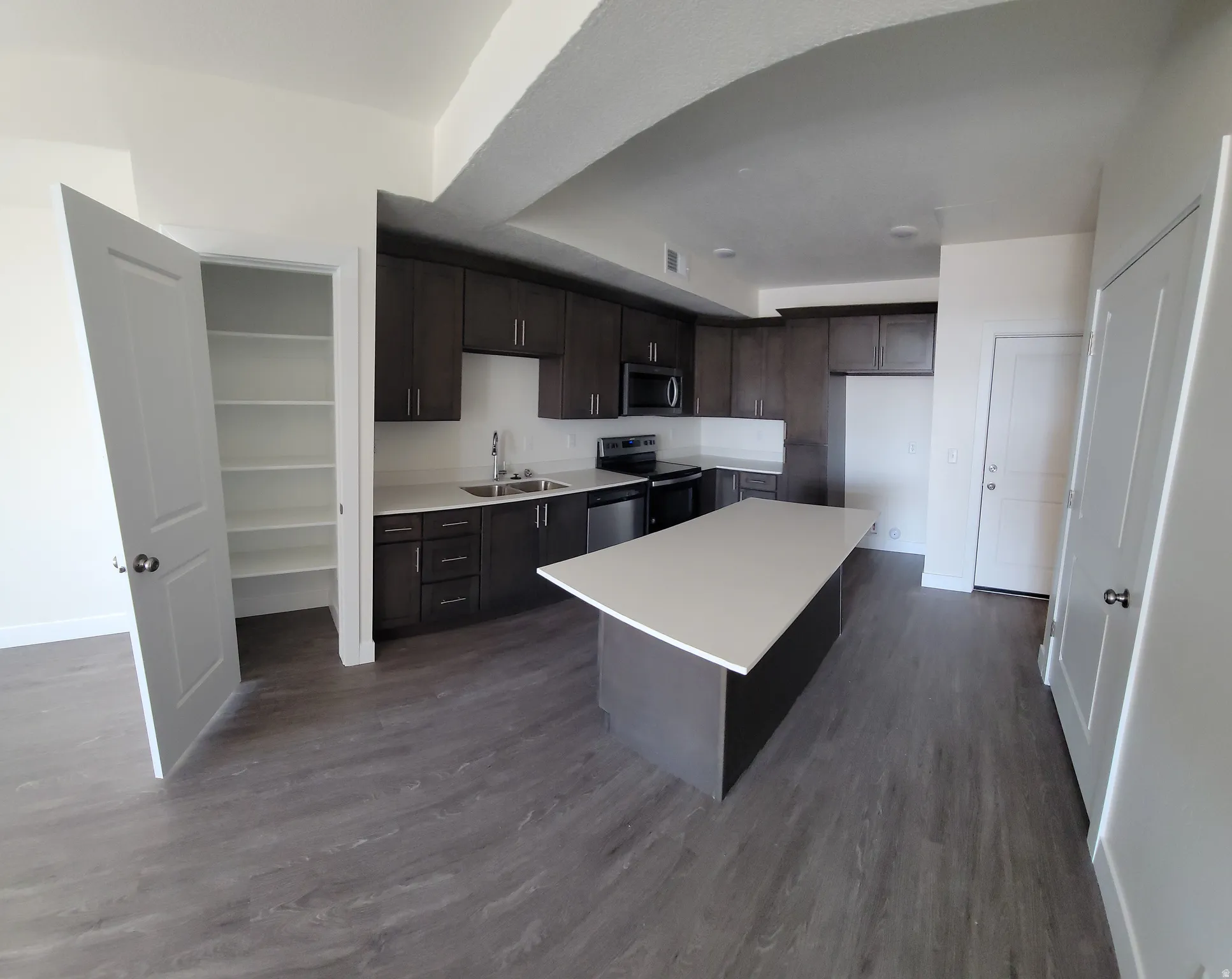 Kitchen with dark wood finish cabinets, light countertops, stainless steel appliances, dark wood finished floors, and a center island