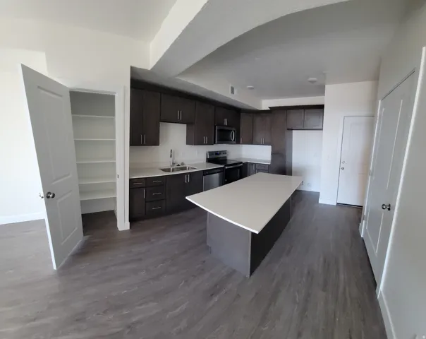 Kitchen with dark wood finish cabinets, light countertops, stainless steel appliances, dark wood finished floors, and a center island