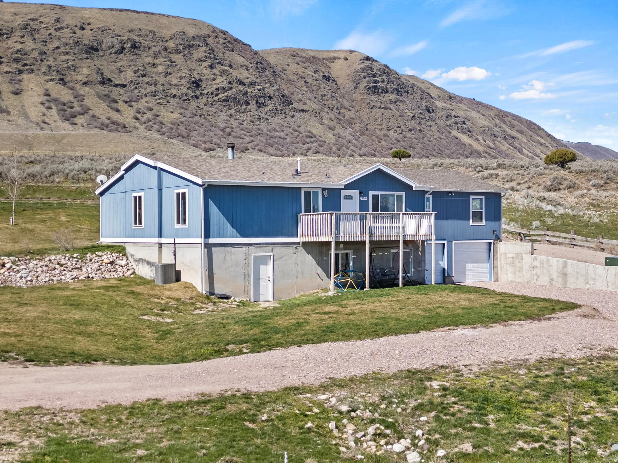 Rear view of house featuring a garage, driveway, a lawn, and a deck with mountain view