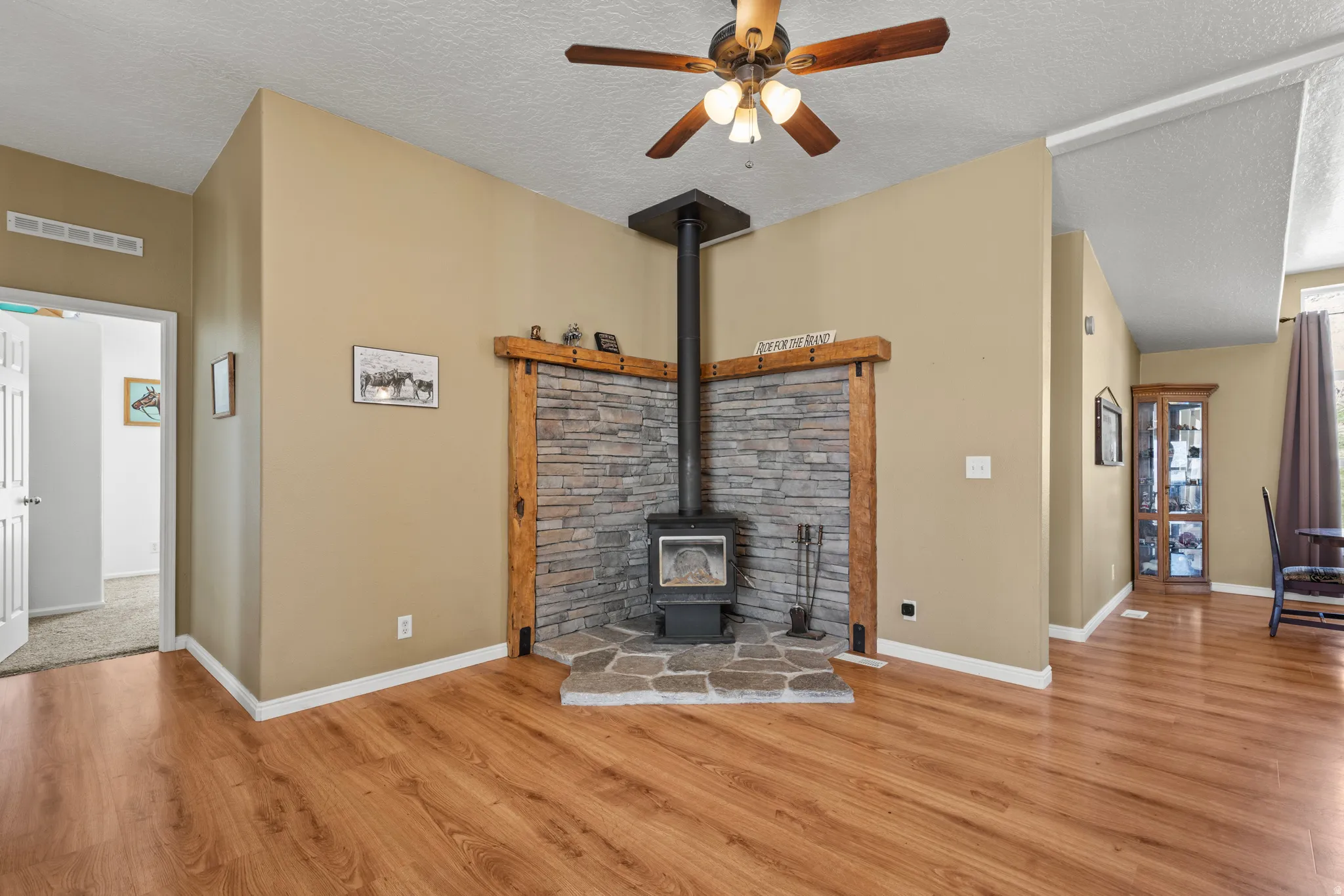 Unfurnished living room featuring a wood stove, a textured ceiling, a ceiling fan, and light wood-style floors