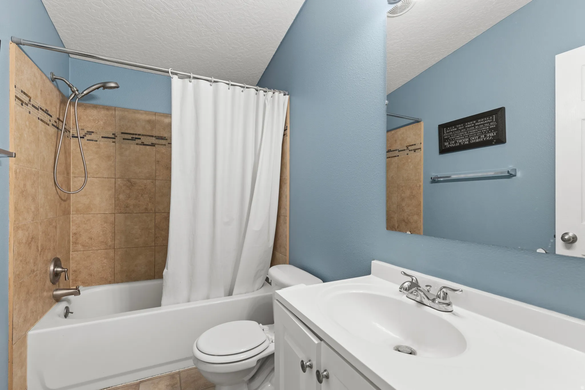 Full bath with vanity, shower / bath combo with shower curtain, a textured ceiling, and a textured wall