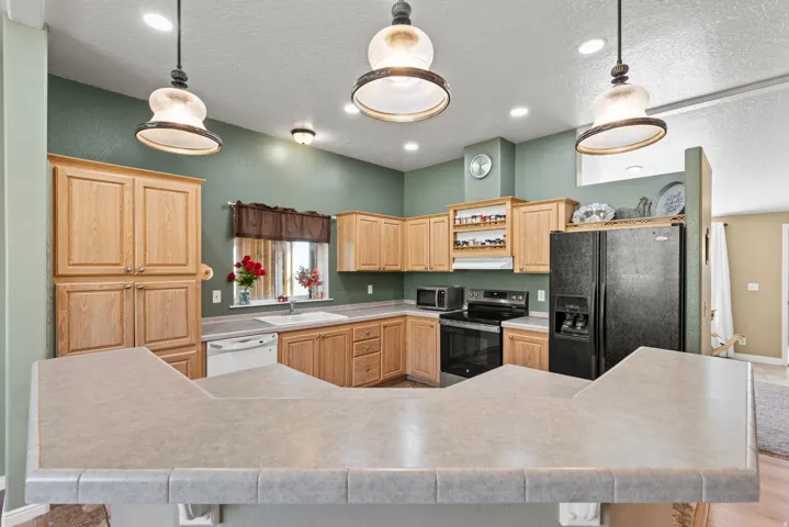 Kitchen with light wood finish cabinets, stainless steel appliances, light countertops, decorative light fixtures, and a textured ceiling