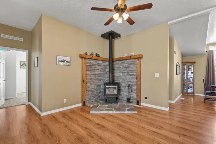 Unfurnished living room featuring a wood stove, a textured ceiling, a ceiling fan, and light wood-style floors