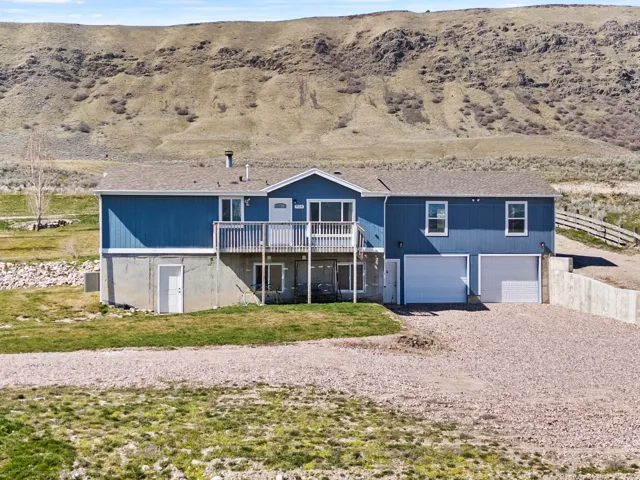 View of front of property with gravel driveway, a garage, a deck, and a shingled roof
