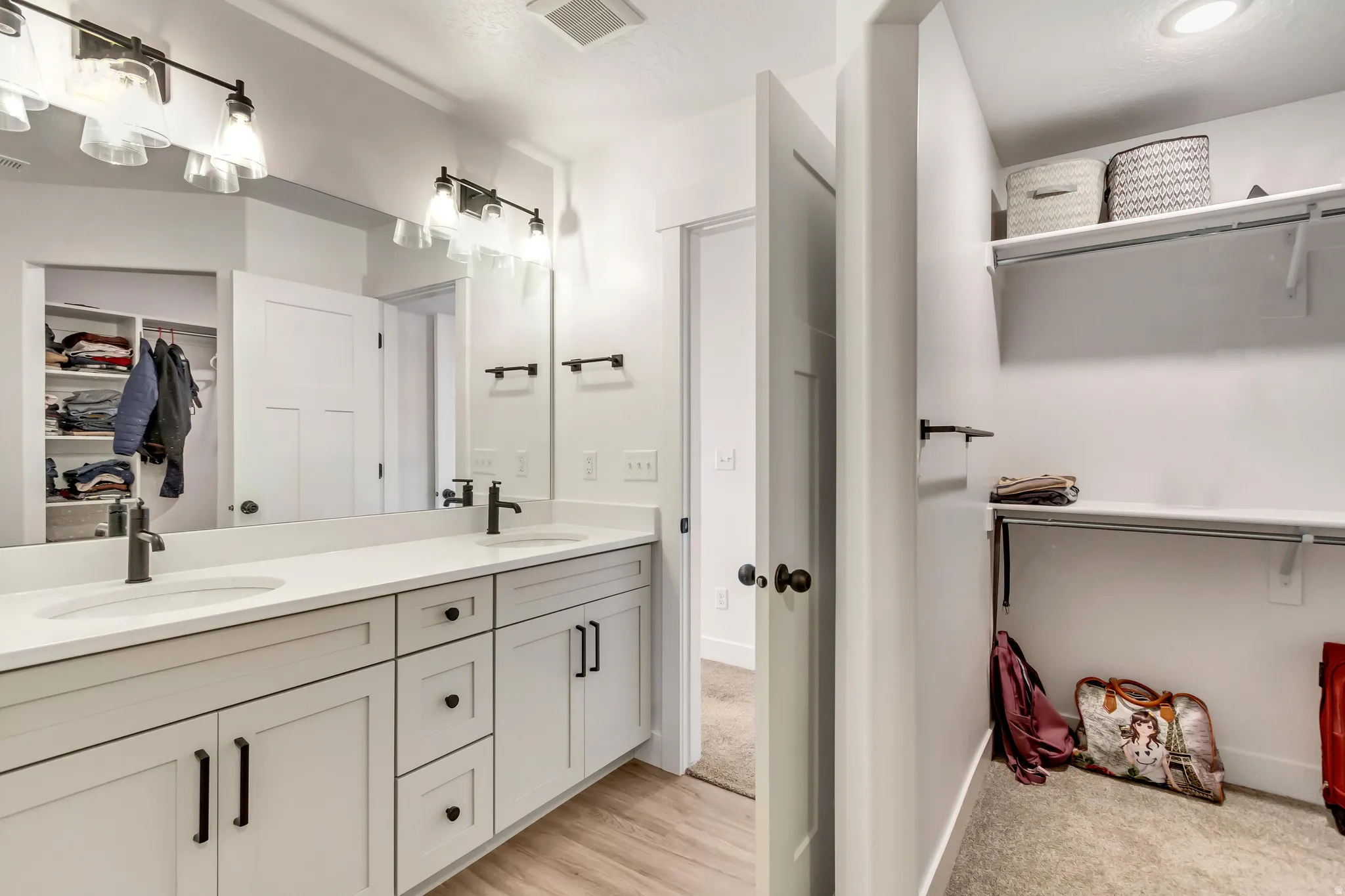 Full bath with a spacious closet, double vanity, and light wood finished floors