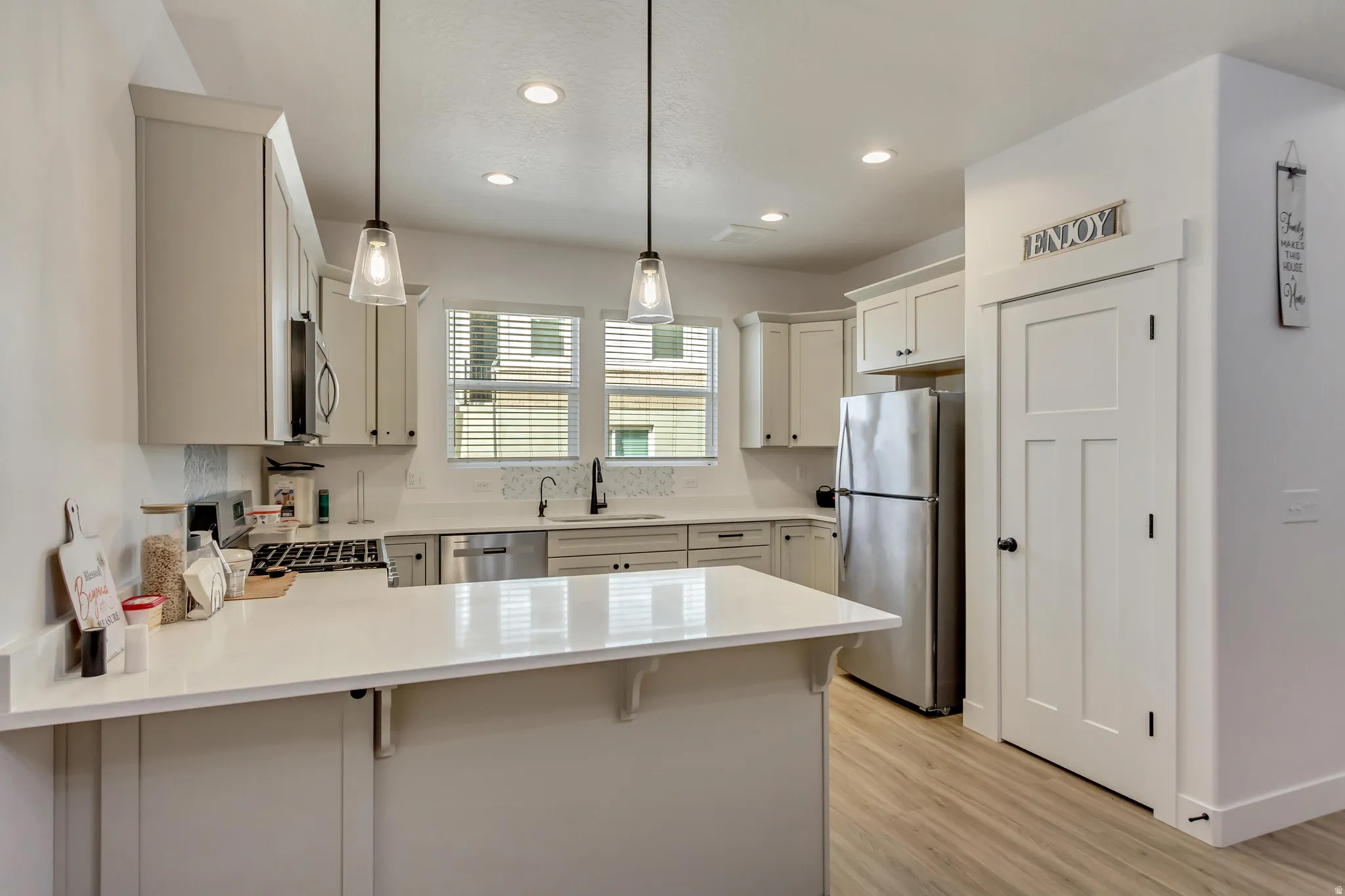 Kitchen featuring a peninsula, a breakfast bar, stainless steel appliances, hanging light fixtures, and light stone countertops