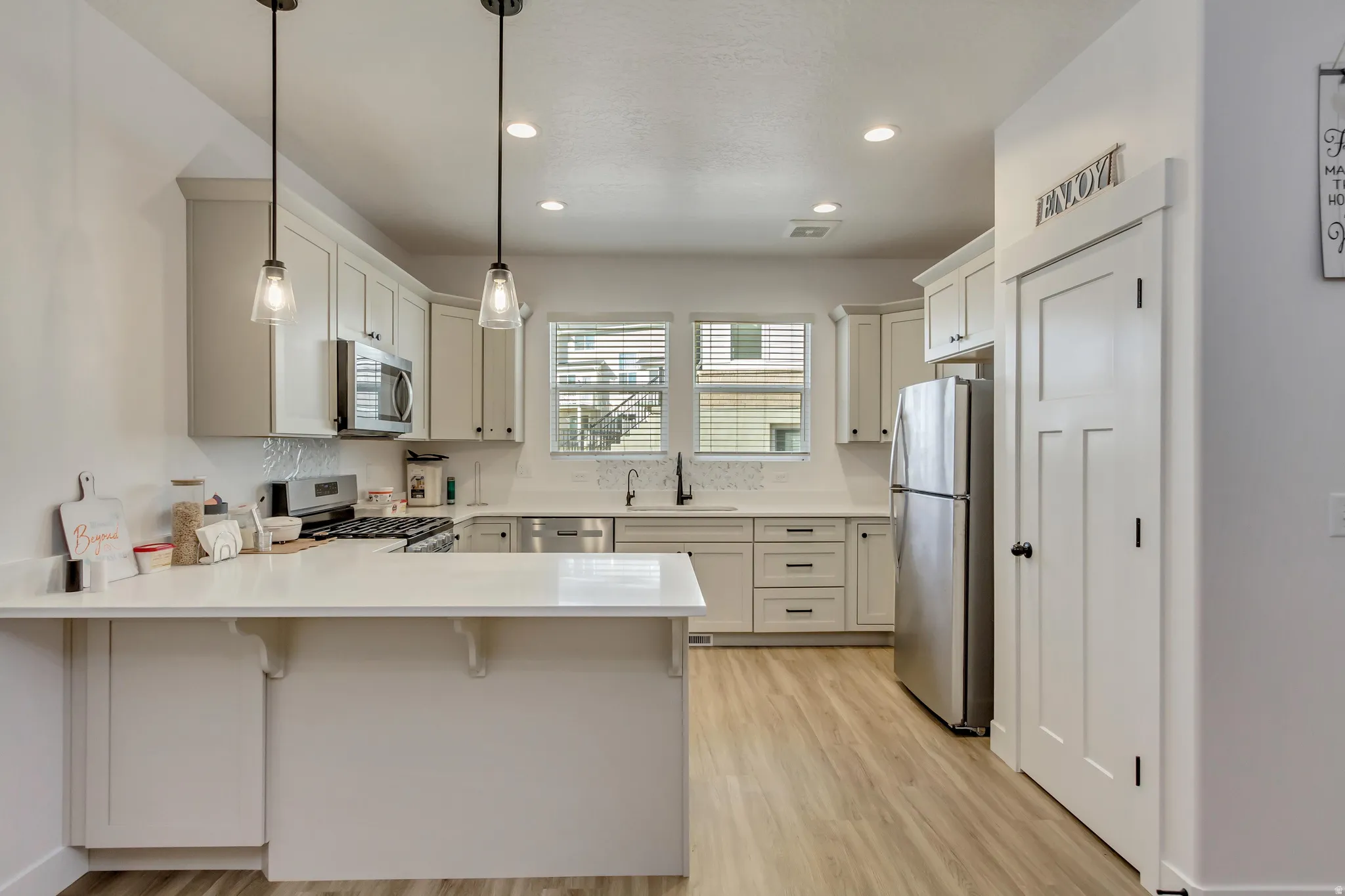 Kitchen with a peninsula, stainless steel appliances, a kitchen bar, light wood-style flooring, and decorative light fixtures