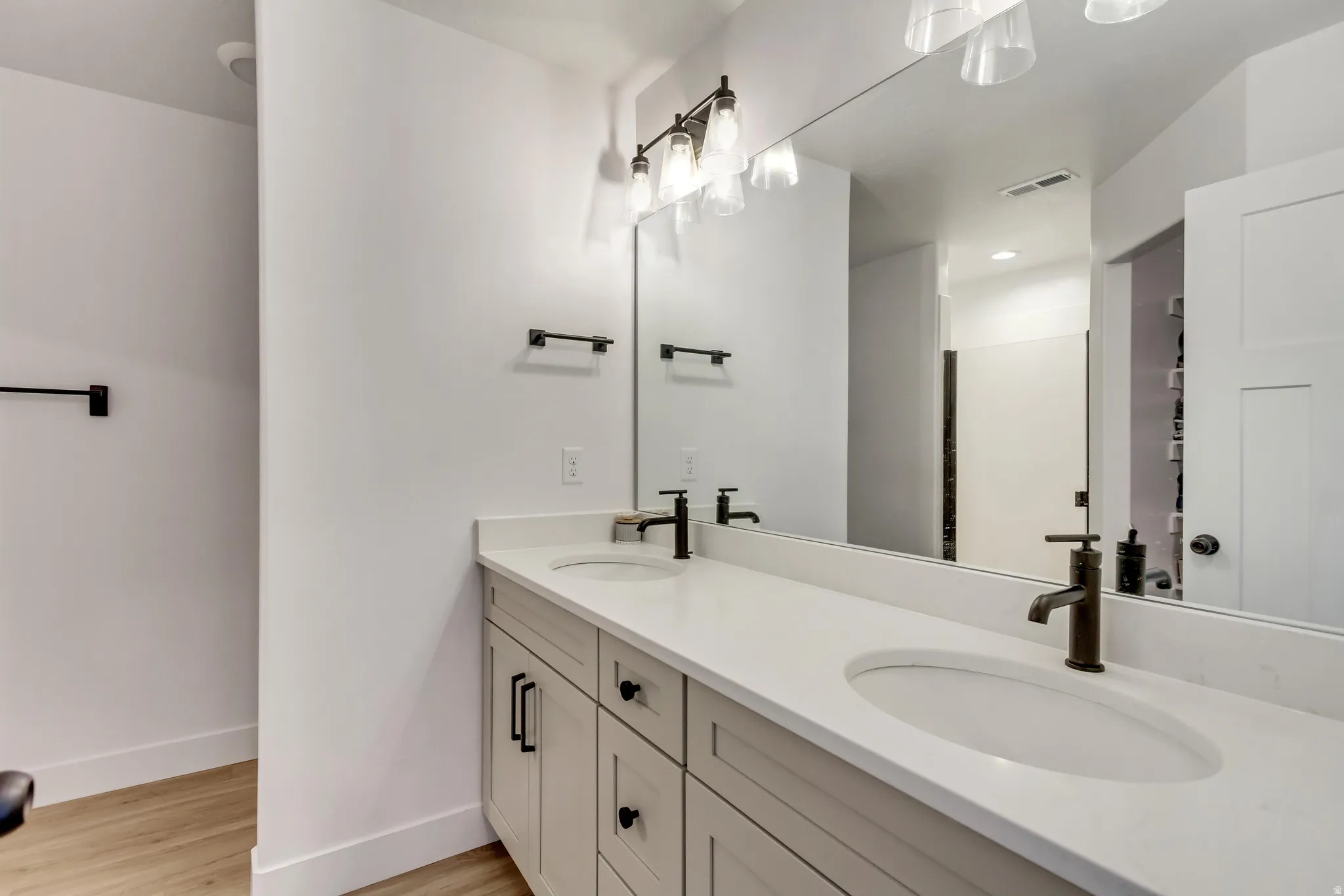 Full bath with double vanity, light wood-type flooring, and a shower