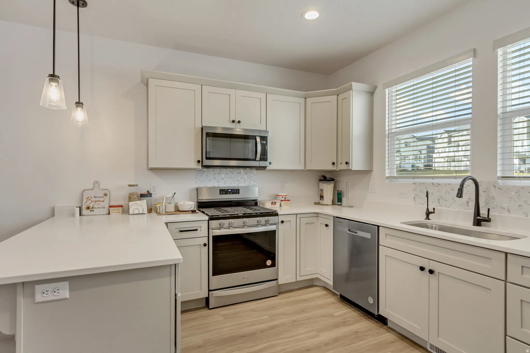 Kitchen featuring a peninsula, stainless steel appliances, light wood-style floors, pendant lighting, and white cabinets