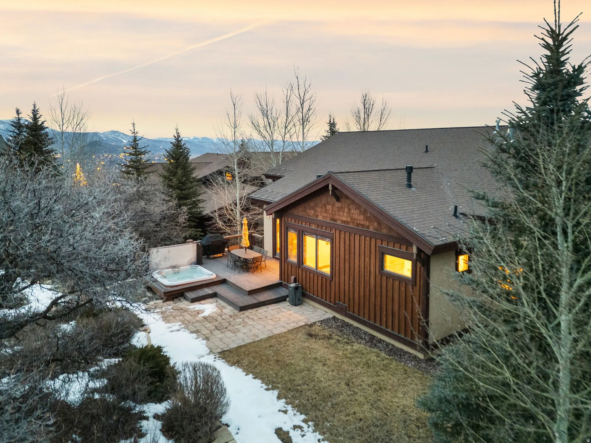 Back of property at dusk with a deck, a hot tub, roof with shingles, and board and batten siding