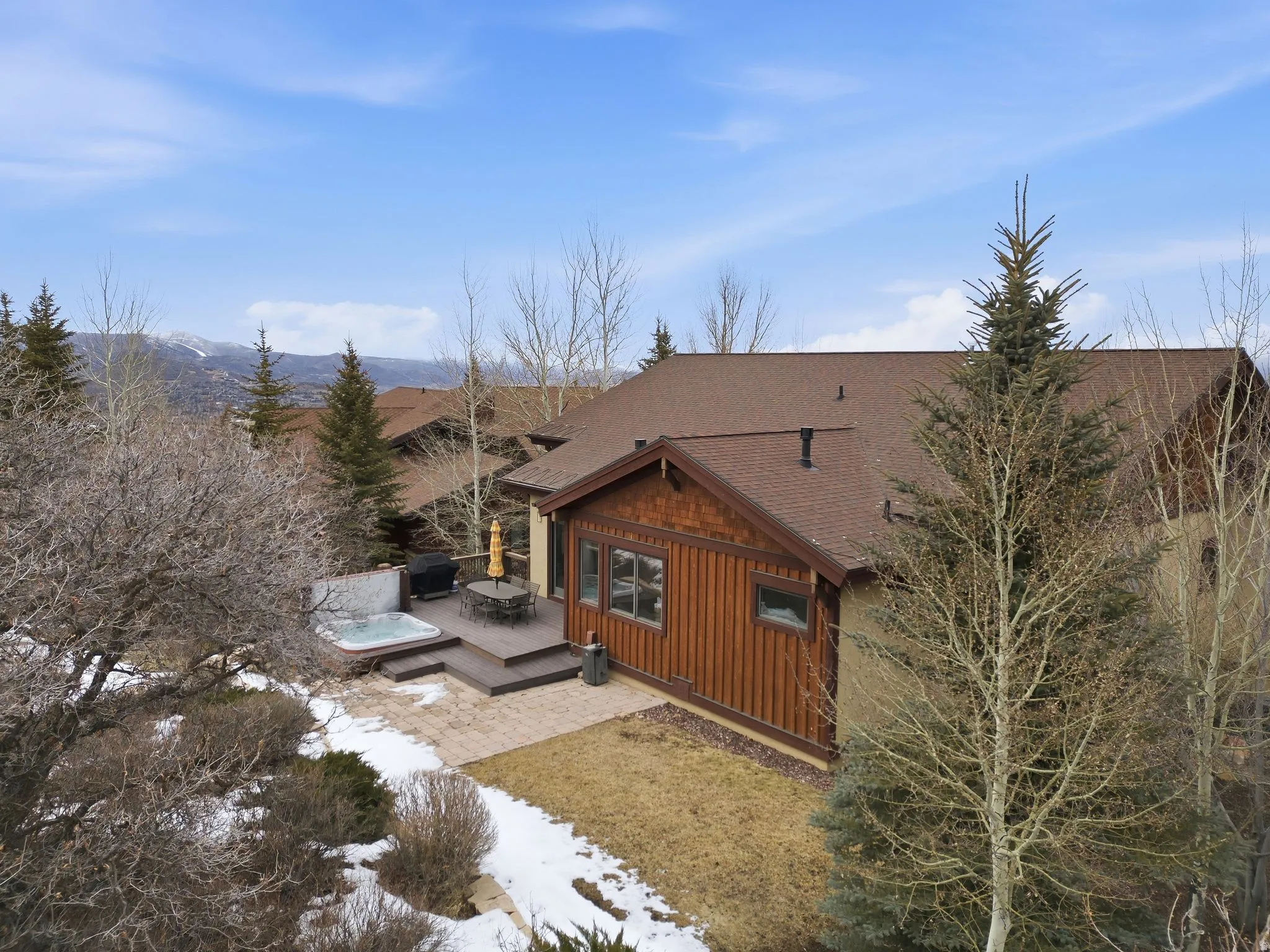 View of side of property with a shingled roof, a hot tub, board and batten siding, a patio area, and a deck