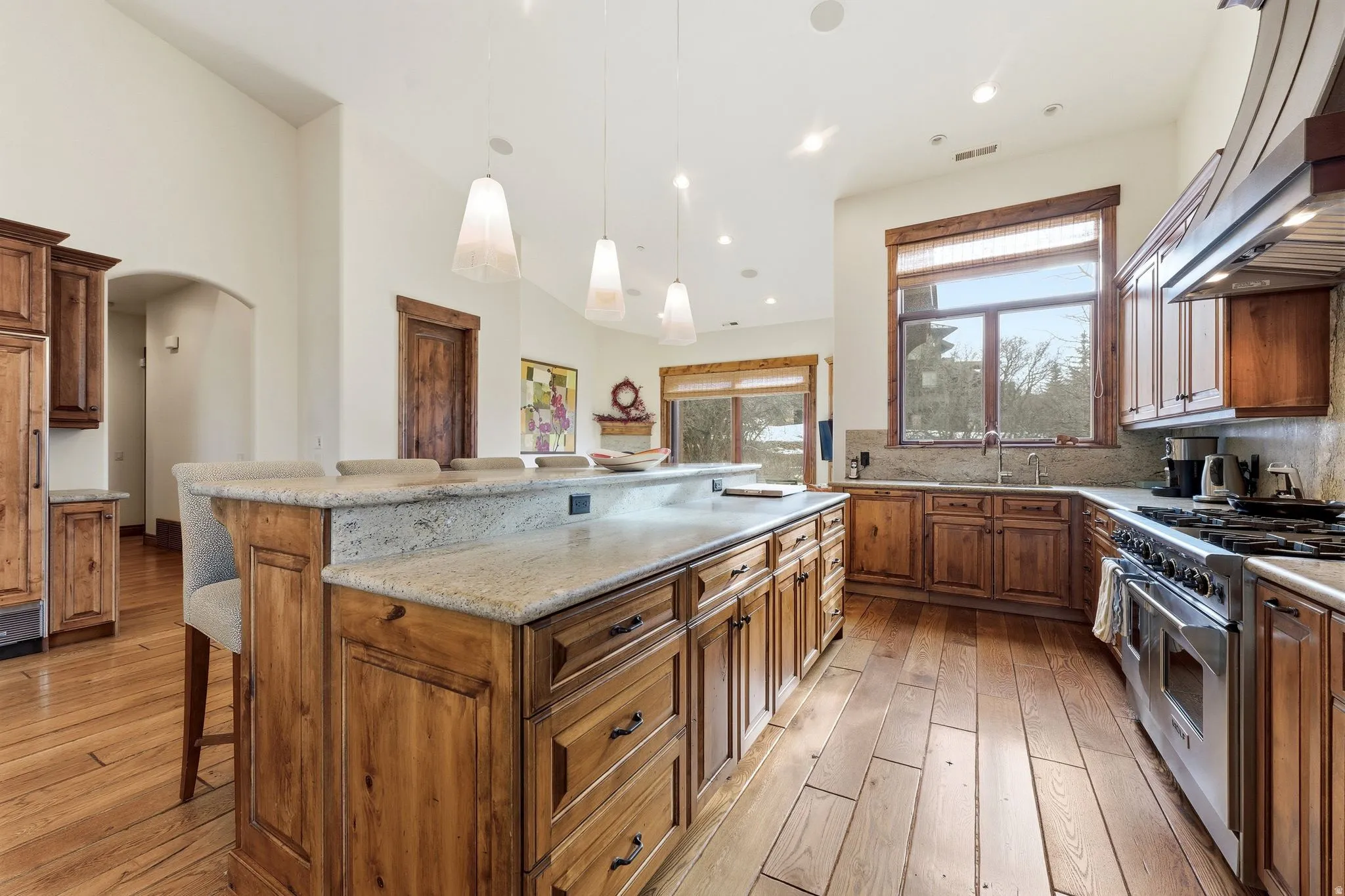 Kitchen featuring a breakfast bar area, wood finish cabinets, double oven range, light wood-style flooring, and arched walkways