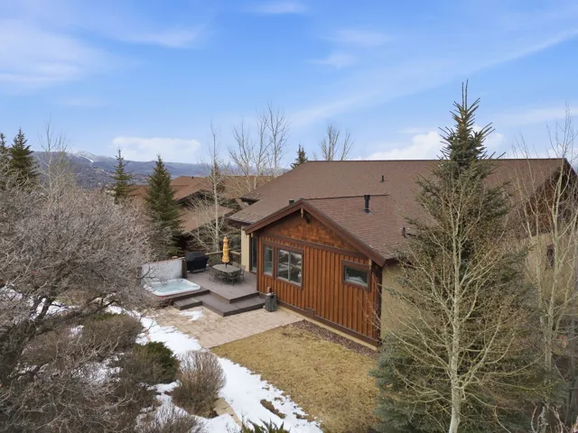 View of side of property with a shingled roof, a hot tub, board and batten siding, a patio area, and a deck