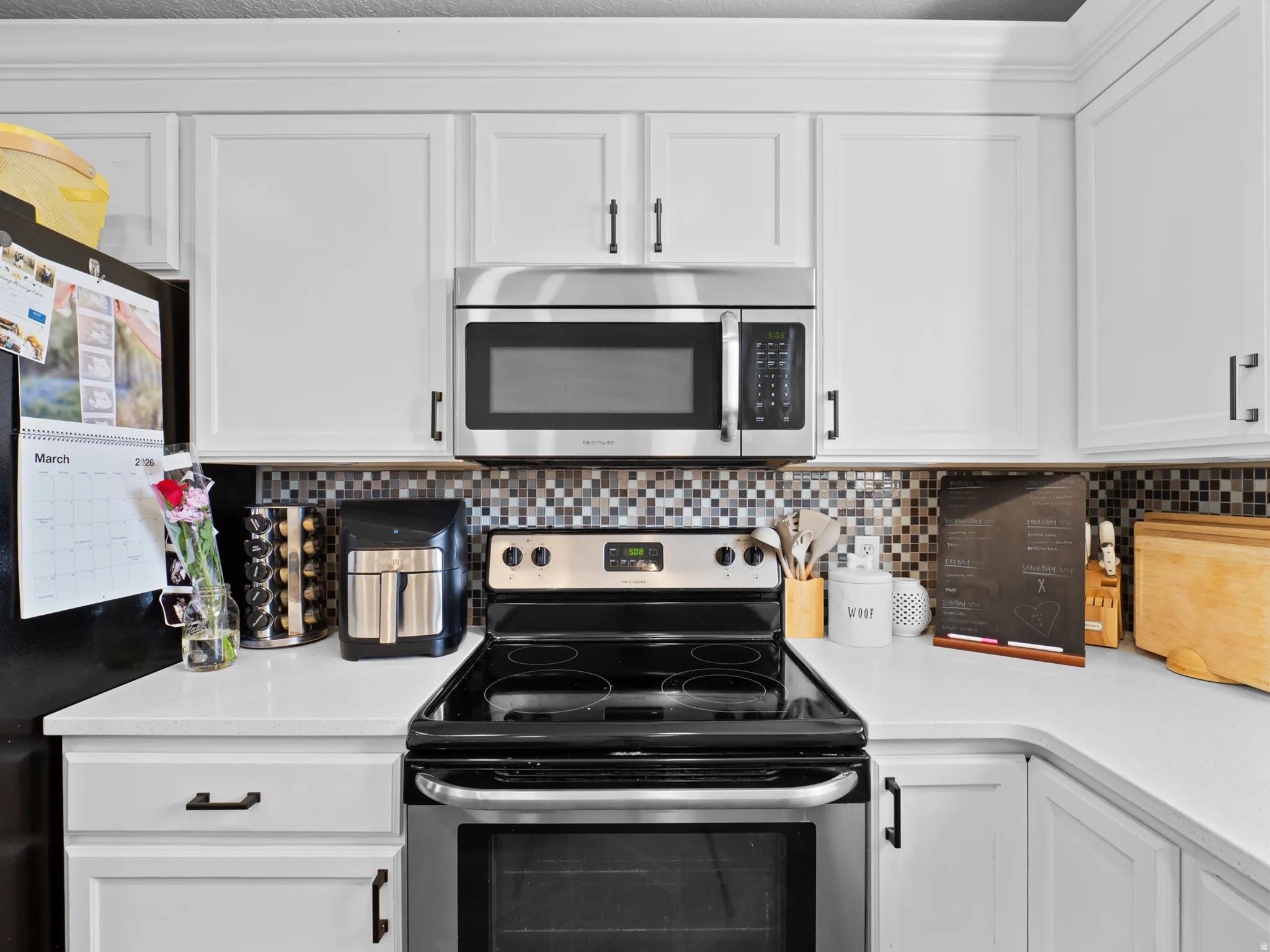 Kitchen with stainless steel appliances, white cabinetry, decorative backsplash, and light stone countertops