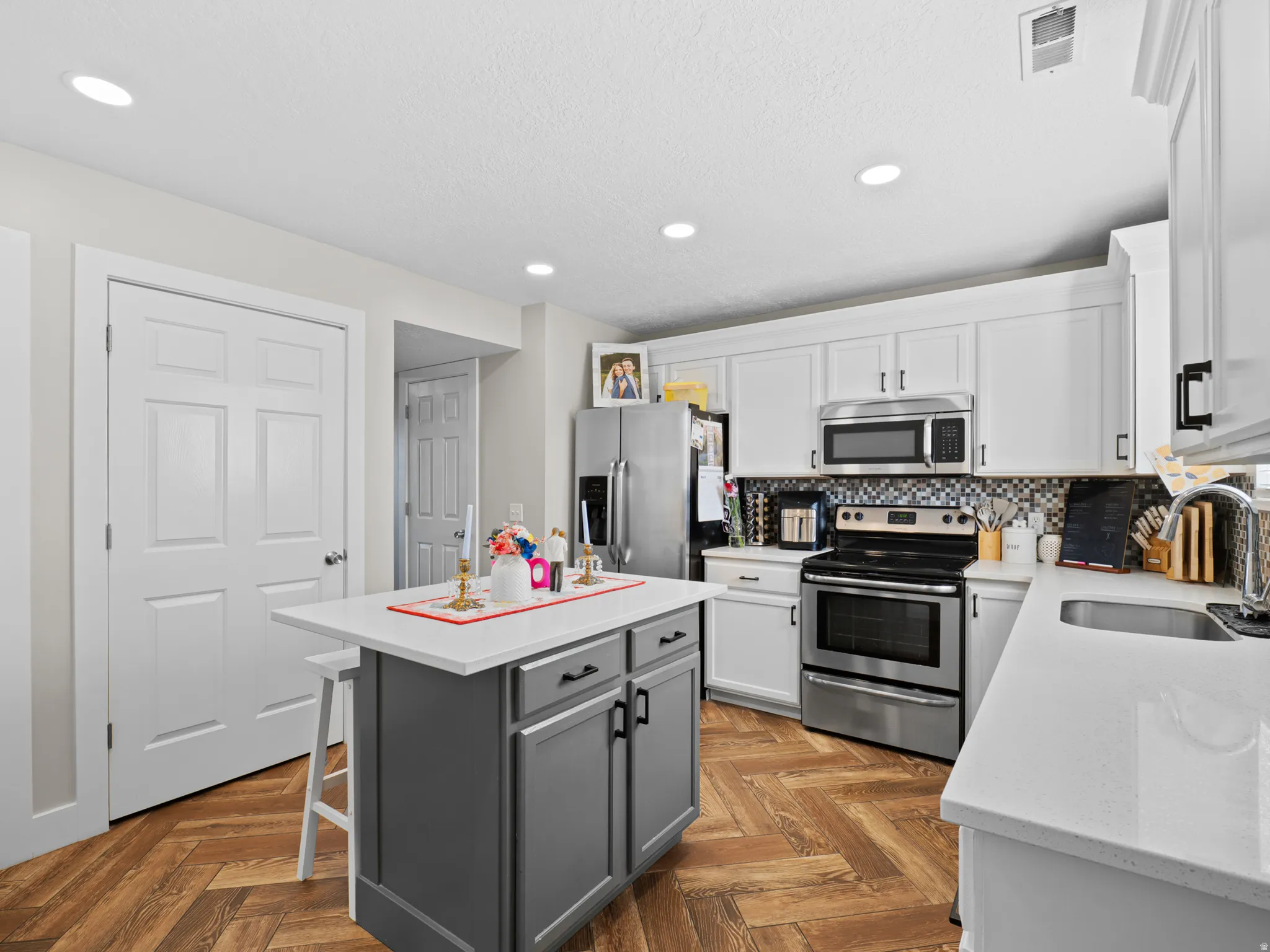 Dual tone kitchen featuring stainless steel appliances, a kitchen island, parquet flooring, backsplash, and recessed lighting