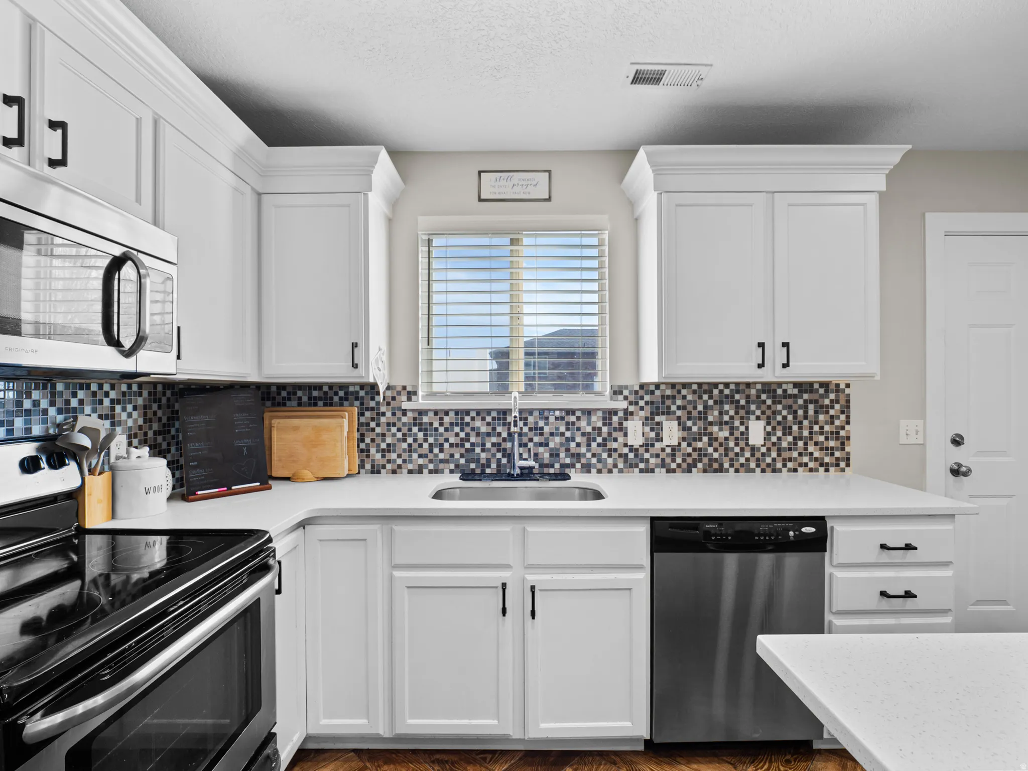 Kitchen featuring stainless steel appliances, white cabinets, a textured ceiling, and tasteful backsplash