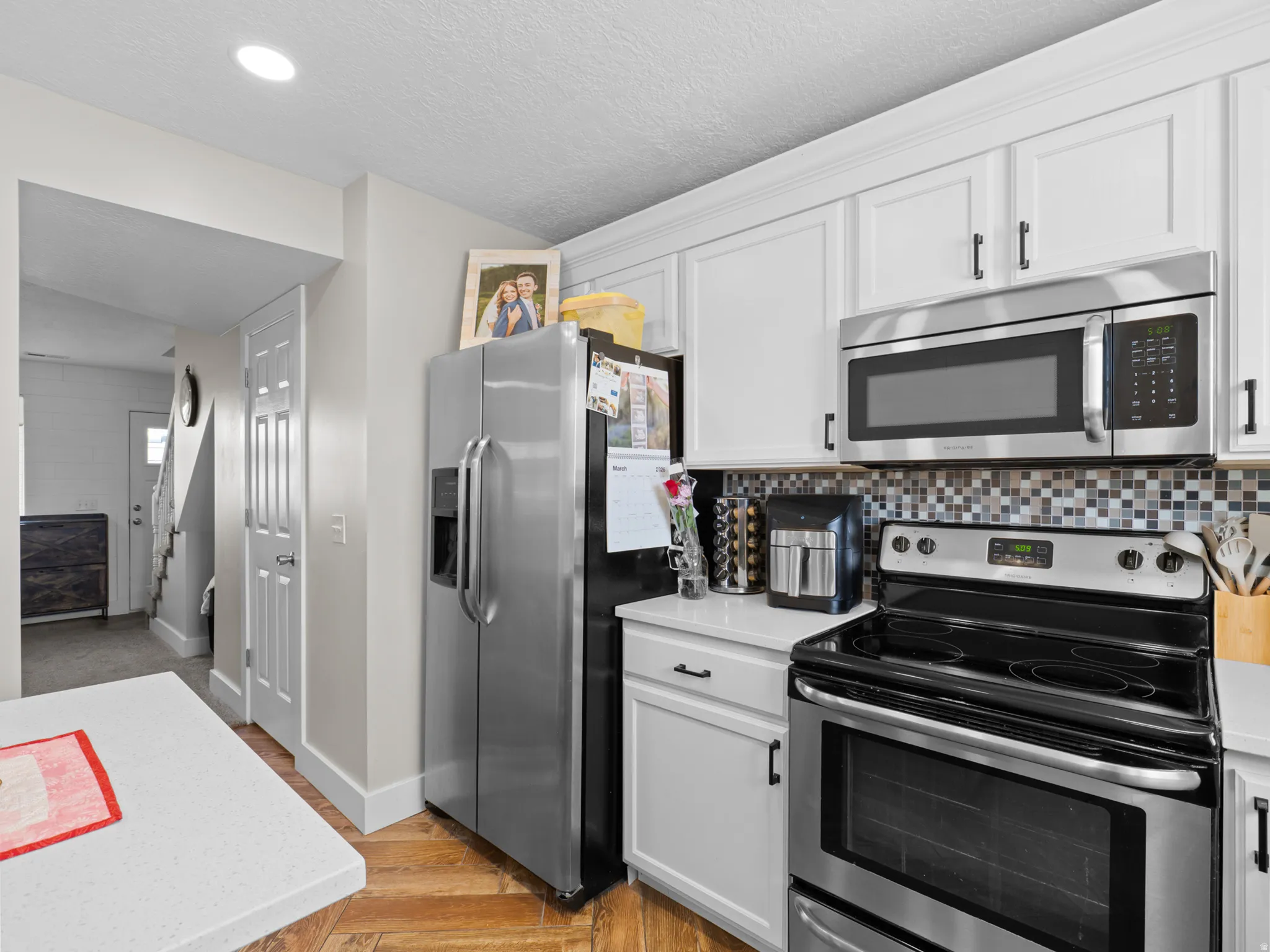 Kitchen with stainless steel appliances, white cabinets, light wood-style flooring, a textured ceiling, and backsplash