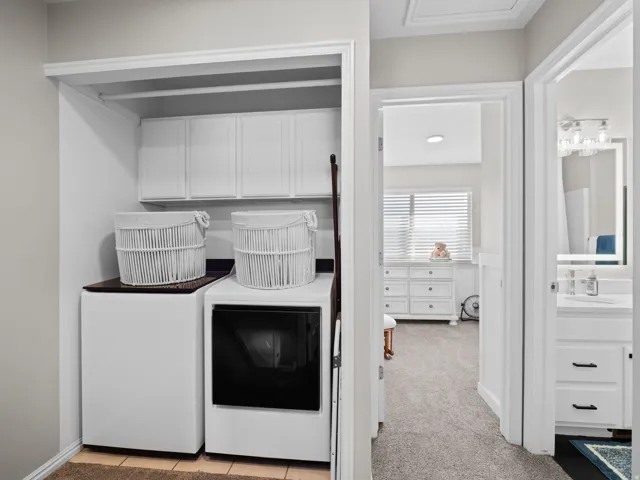 Laundry area featuring light colored carpet, cabinet space, and washing machine and clothes dryer