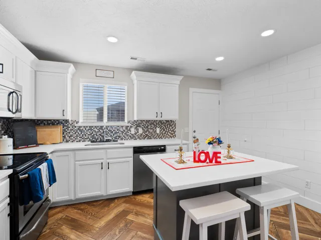 Two tone kitchen featuring stainless steel appliances, a breakfast bar area, a kitchen island, parquet flooring, and recessed lighting