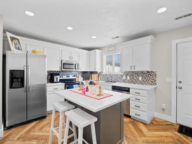 Two tone kitchen with stainless steel appliances, a center island, a kitchen breakfast bar, parquet flooring, and recessed lighting