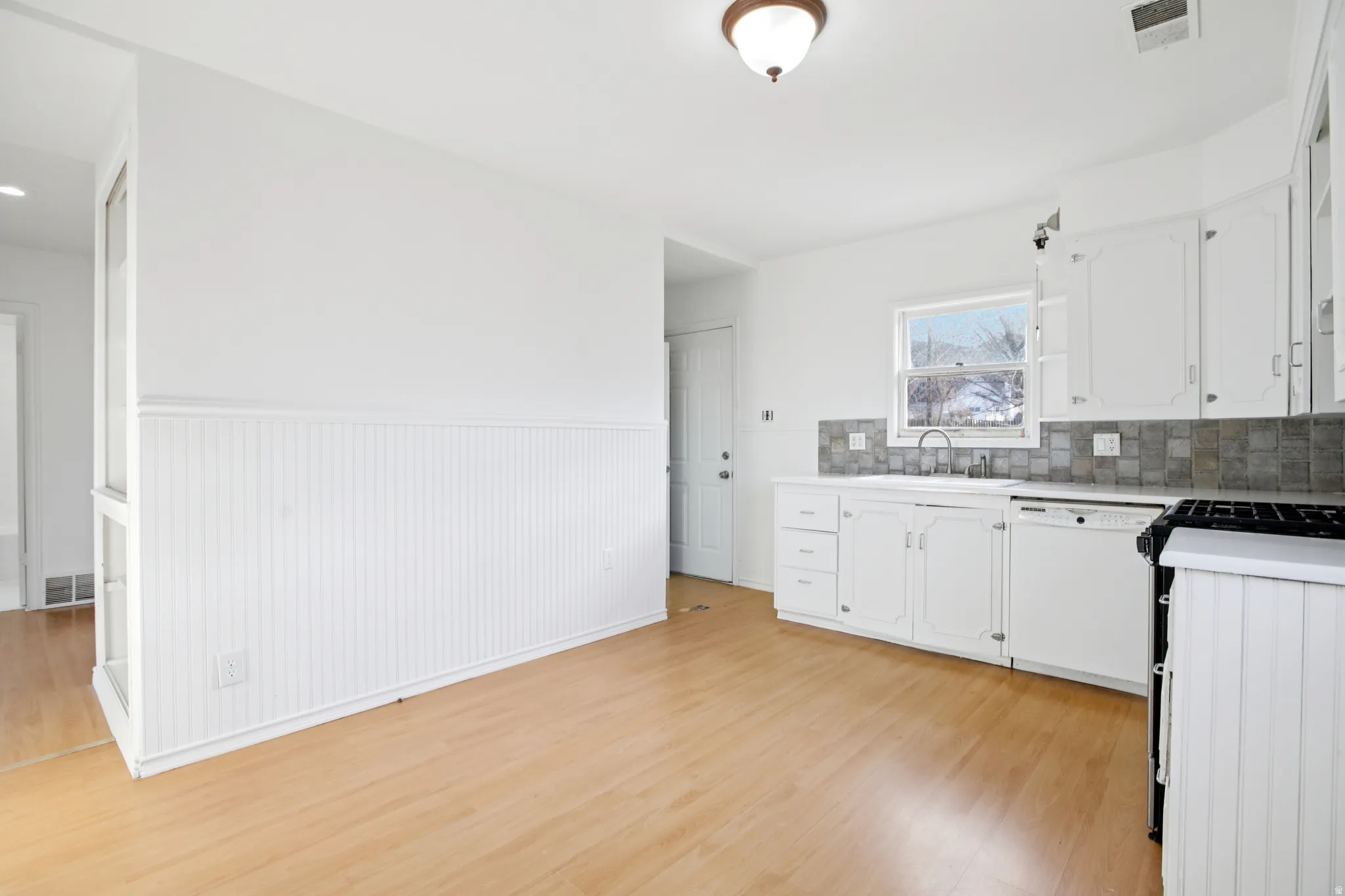 Kitchen with light countertops, a wainscoted wall, white cabinetry, white dishwasher, and range with gas stovetop
