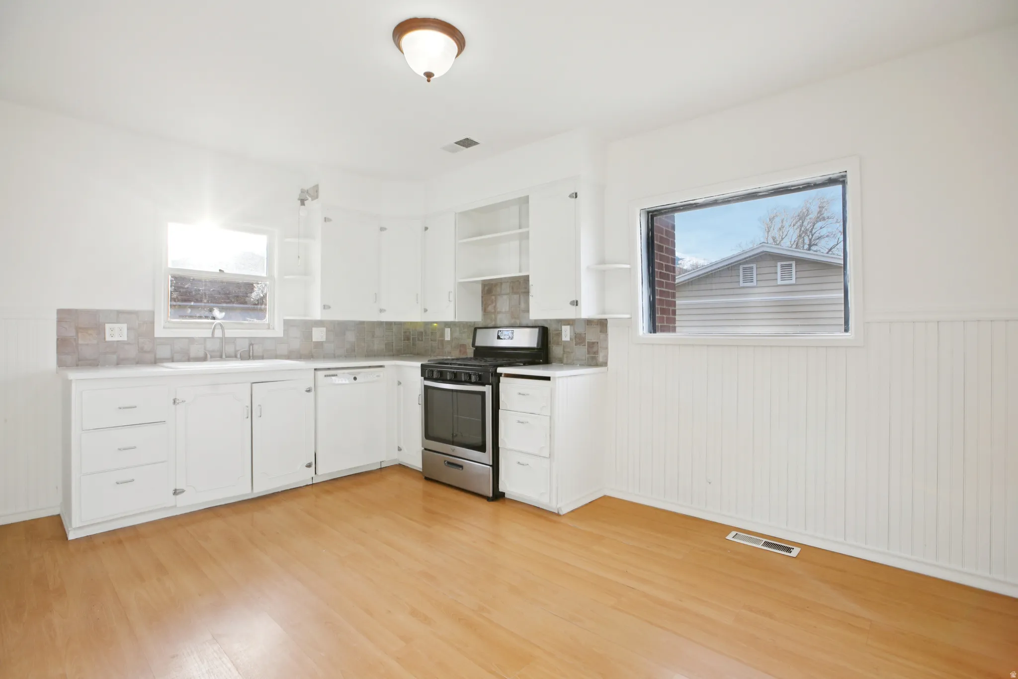 Kitchen featuring wainscoting, stainless steel gas range, light countertops, dishwasher, and white cabinets