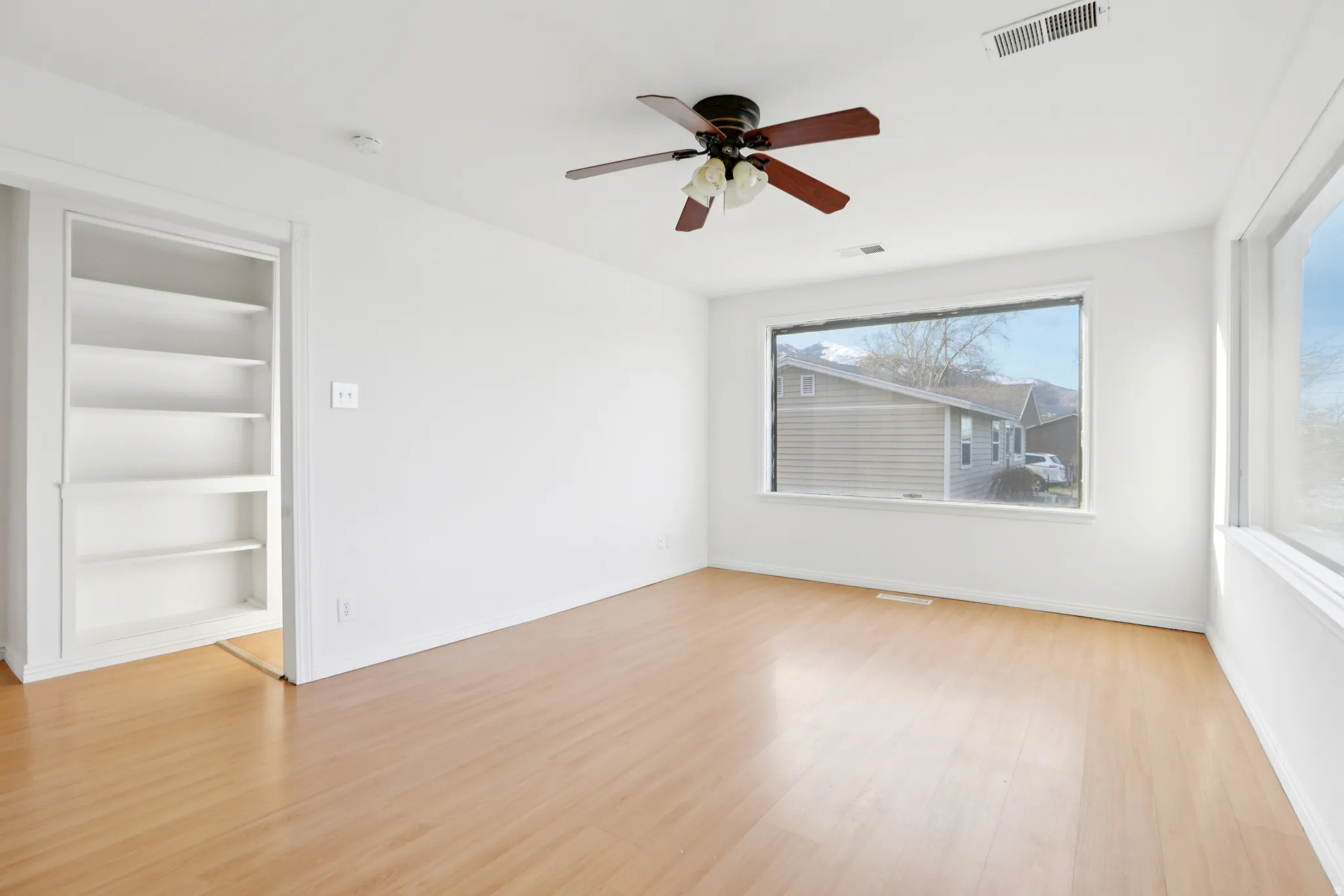 Spare room featuring built in shelves, ceiling fan, and light wood finished floors